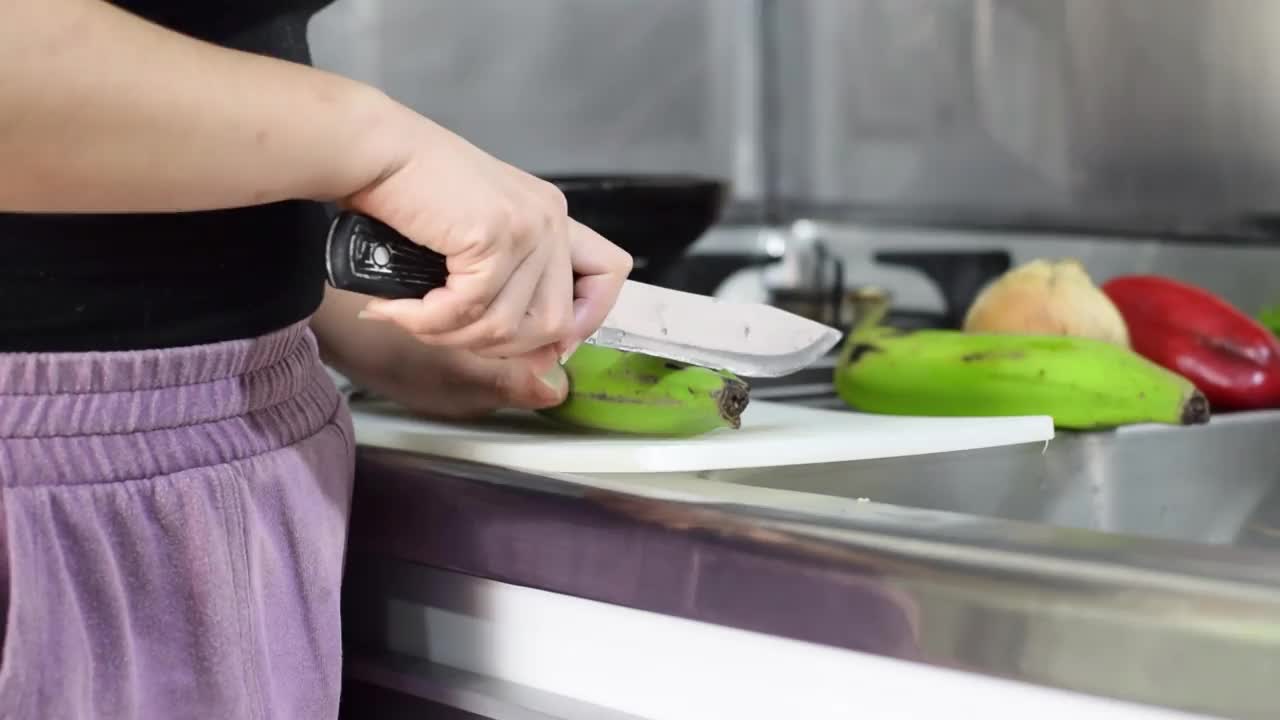 一名妇女在厨房用刀切绿香蕉准备食物的详细视图。视频素材