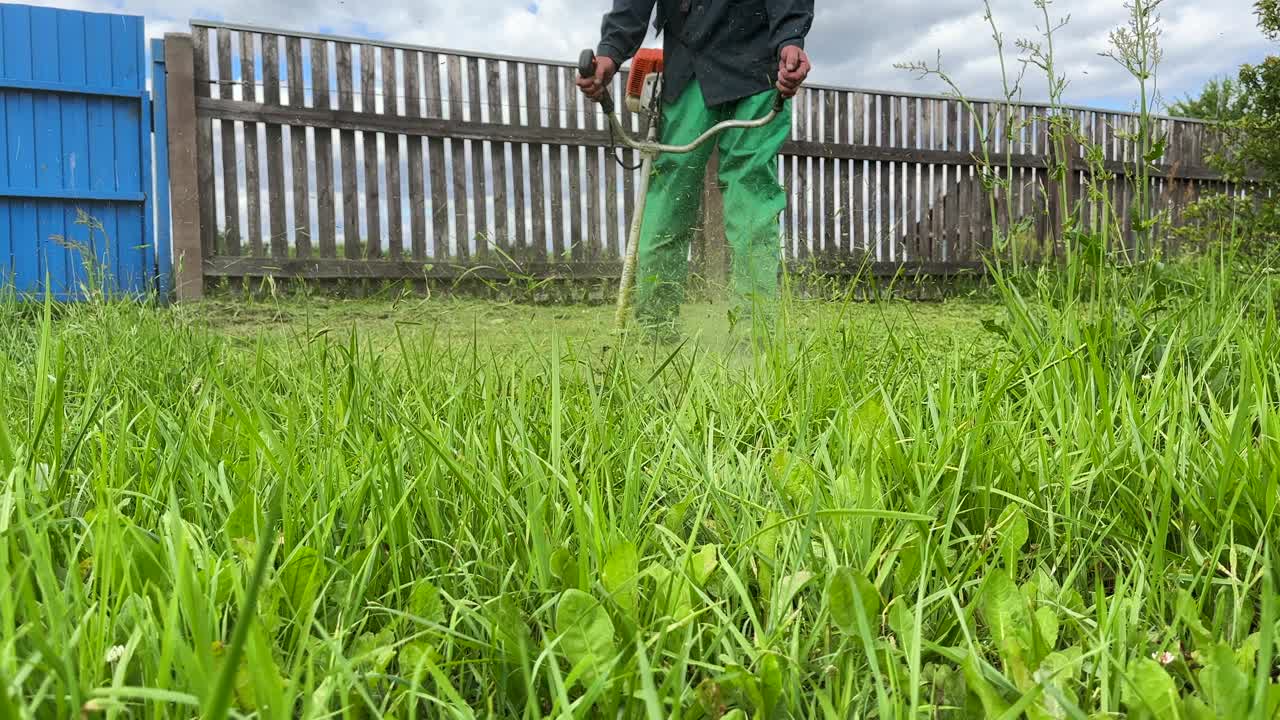 园丁修剪杂草。一个人在院子里用剪绳机割草。视频素材