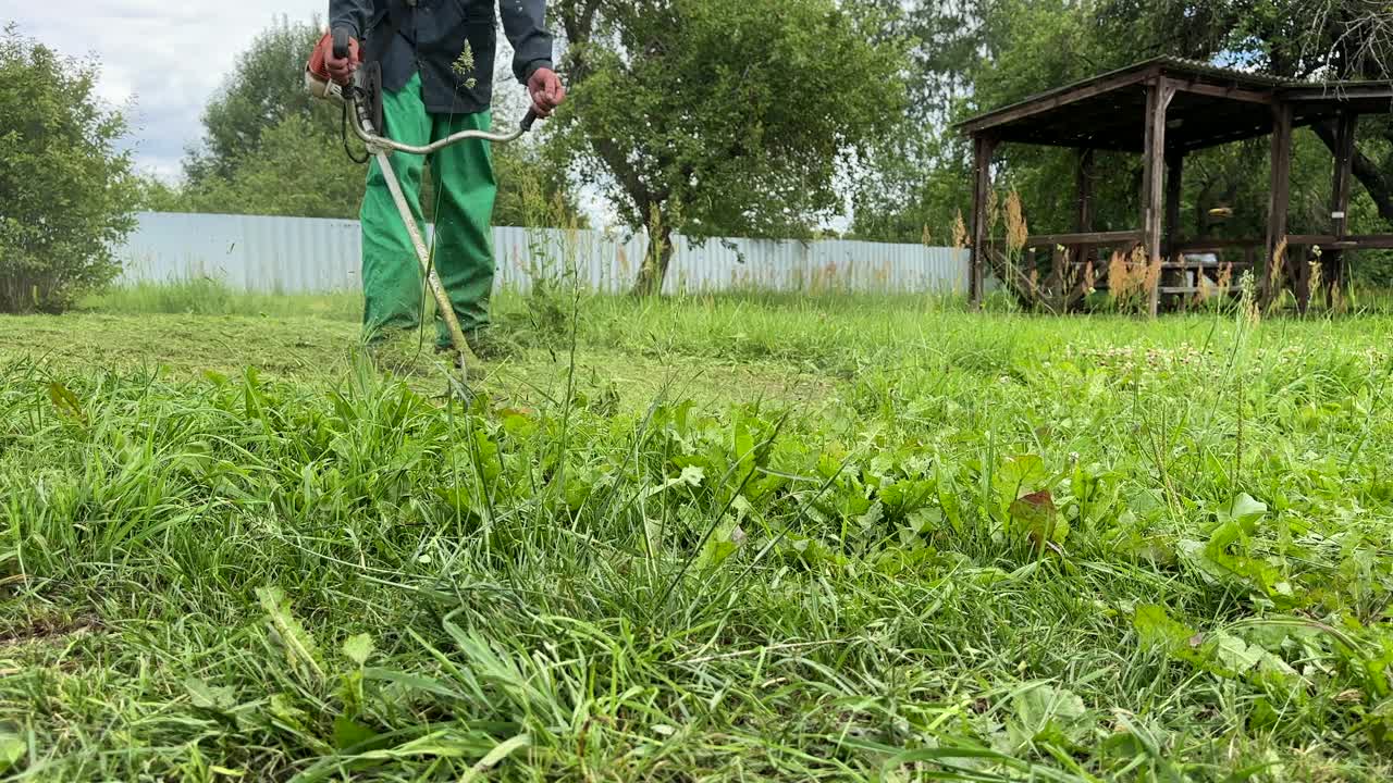 园丁修剪杂草。一个人在院子里用剪绳机割草。视频素材