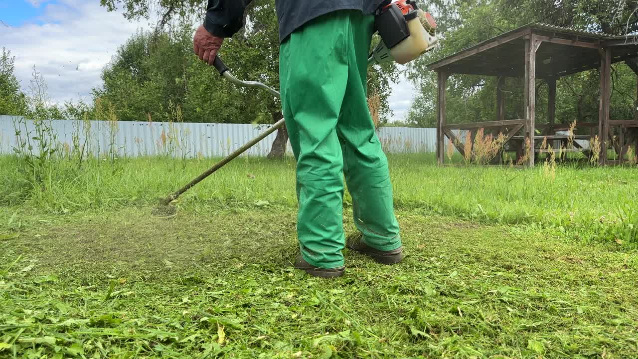 园丁修剪杂草。一个人在院子里用剪绳机割草。视频素材