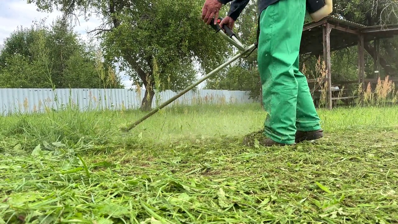 园丁修剪杂草。一个人在院子里用剪绳机割草。视频素材