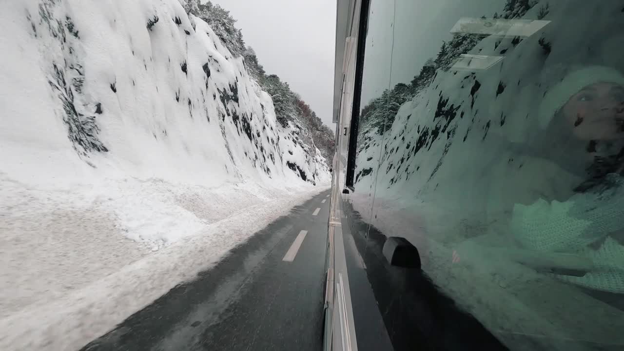 车辆厢式车露营车房车外的乘客窗口视图行驶在雪地冬天的道路与雪山反射在玻璃上。旅行者和度假的概念。Vanlife生活方式。自然视频素材