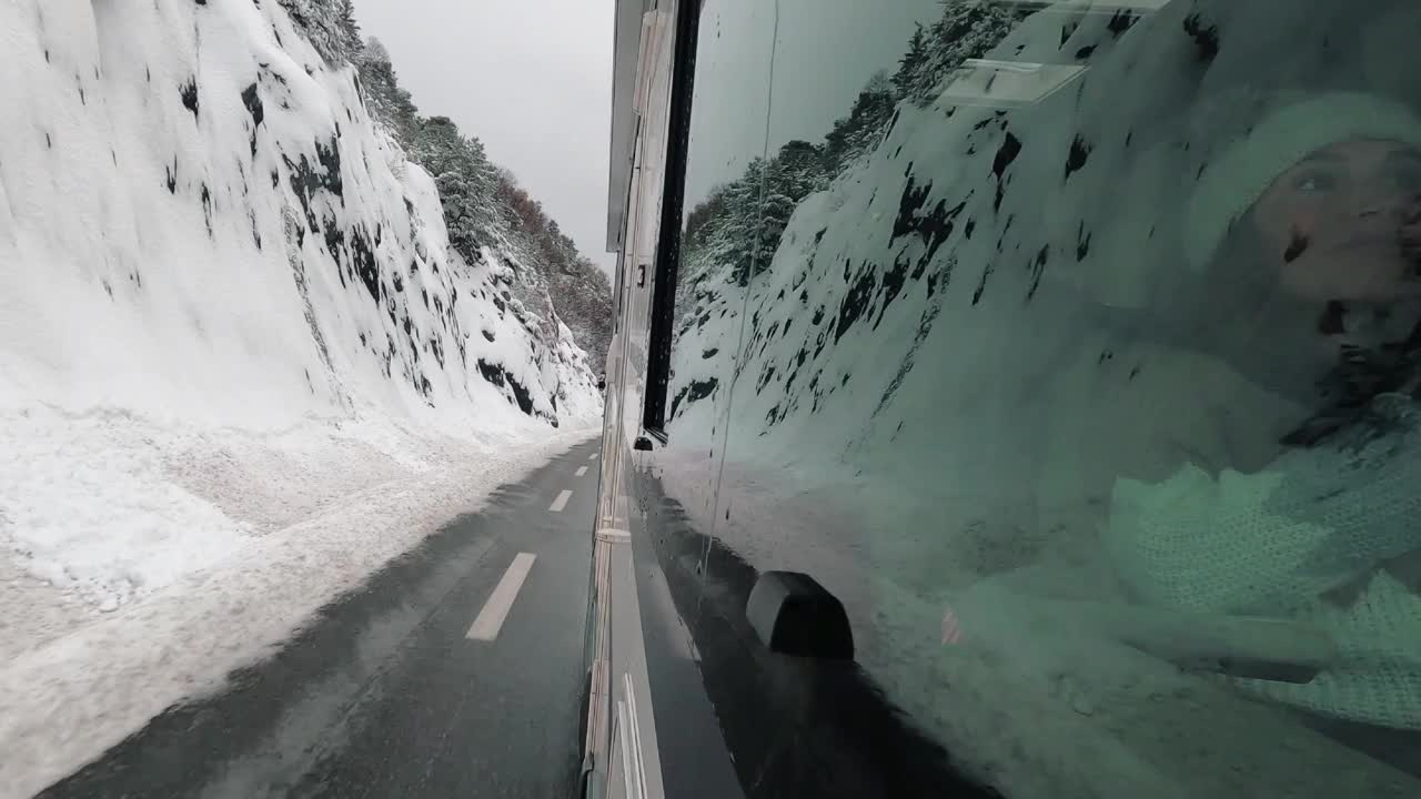 车辆厢式车露营车房车外的乘客窗口视图行驶在雪地冬天的道路与雪山反射在玻璃上。旅行者和度假的概念。Vanlife生活方式。自然视频素材