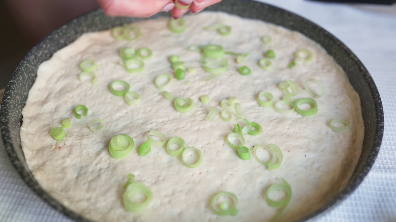 新鲜的韭菜放在烤盘里的披萨面团上。Pizzaiolo做披萨。近距离俯视图的女厨师手准备披萨在家庭厨房。4K视频概念的传统食物和烹饪。视频下载