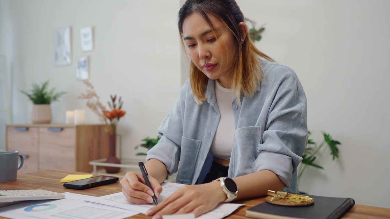 一名亚洲妇女计算每年的个人财务计划预算，并填写美国纳税表格1040视频素材