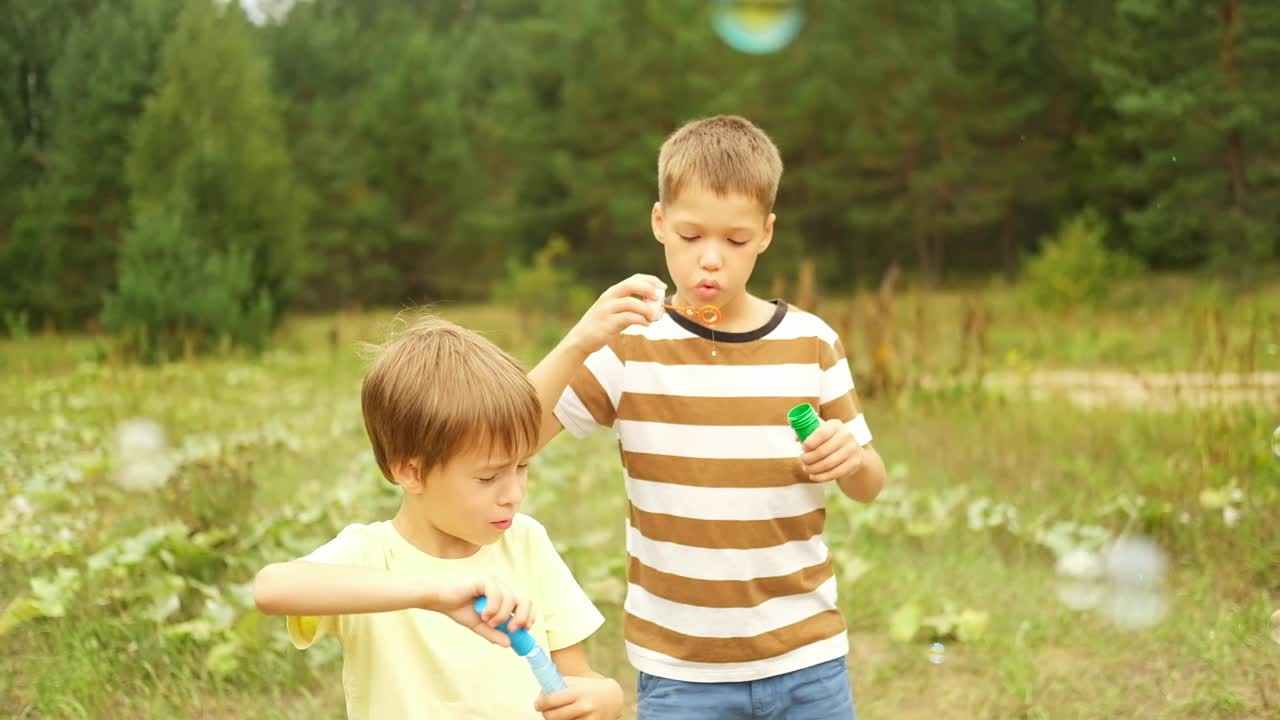 在一个阳光明媚的夏日，男孩们在公园里吹肥皂泡。孩子们周末在户外玩得很开心。视频下载