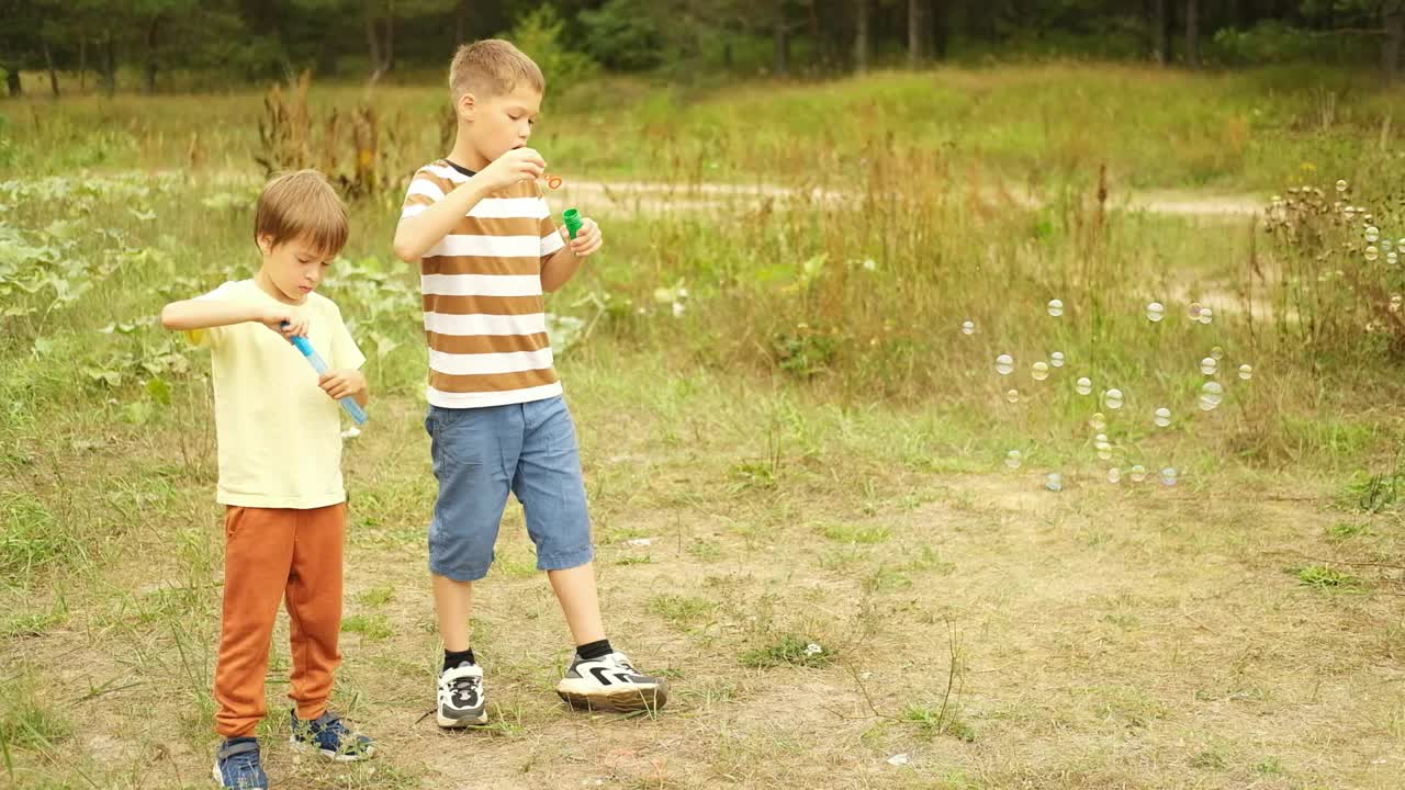 在一个阳光明媚的夏日，男孩们在公园里吹肥皂泡。孩子们周末在户外玩得很开心。视频下载