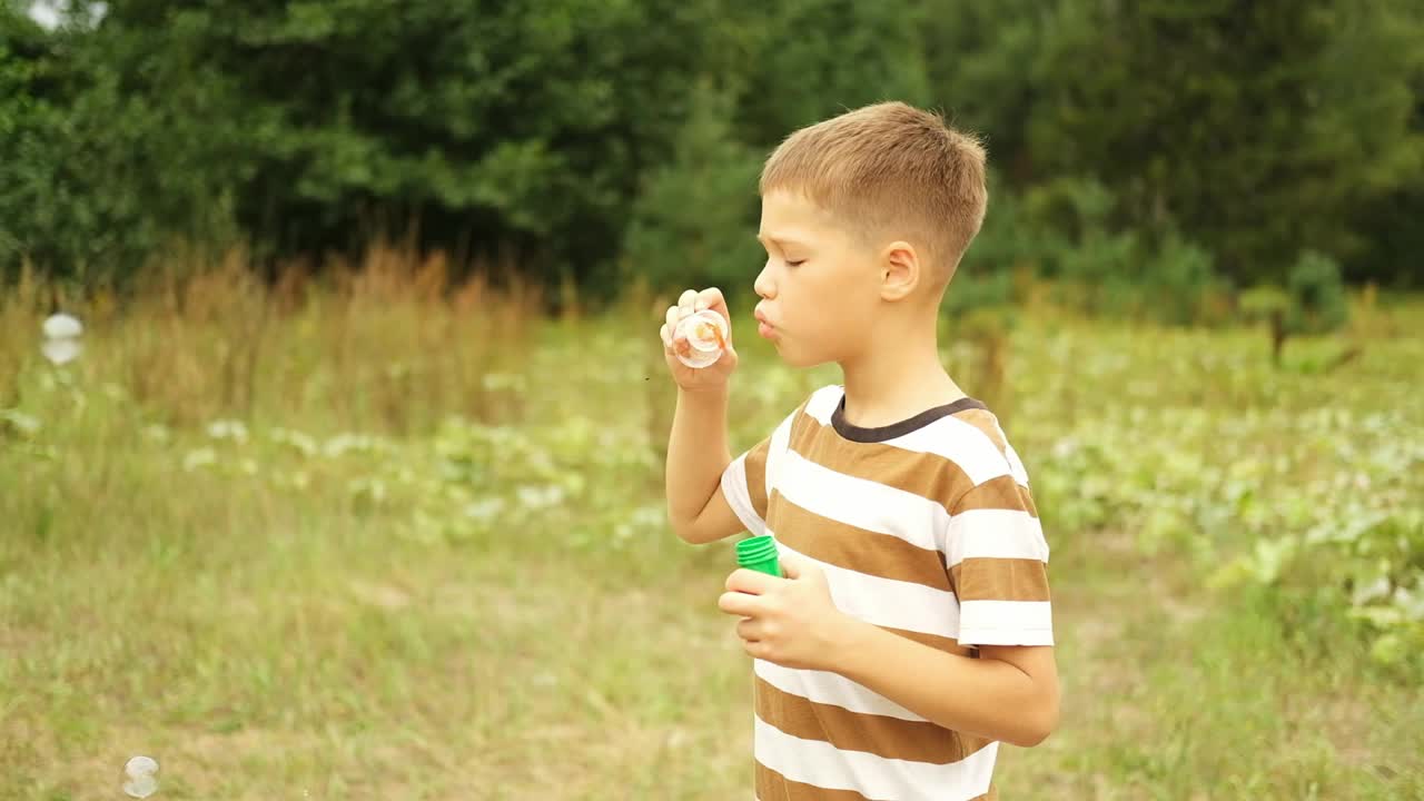 一个白人男孩在夏天的一天在公园散步，吹着肥皂泡。视频下载