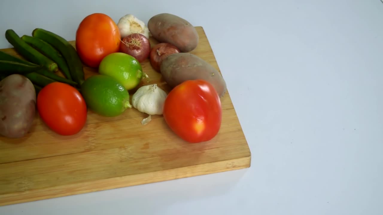 蔬菜放进木质砧板。白色背景的餐桌上有蔬菜和砧板。青菜、西红柿、土豆、大蒜、洋葱等。滑动蔬菜。视频素材