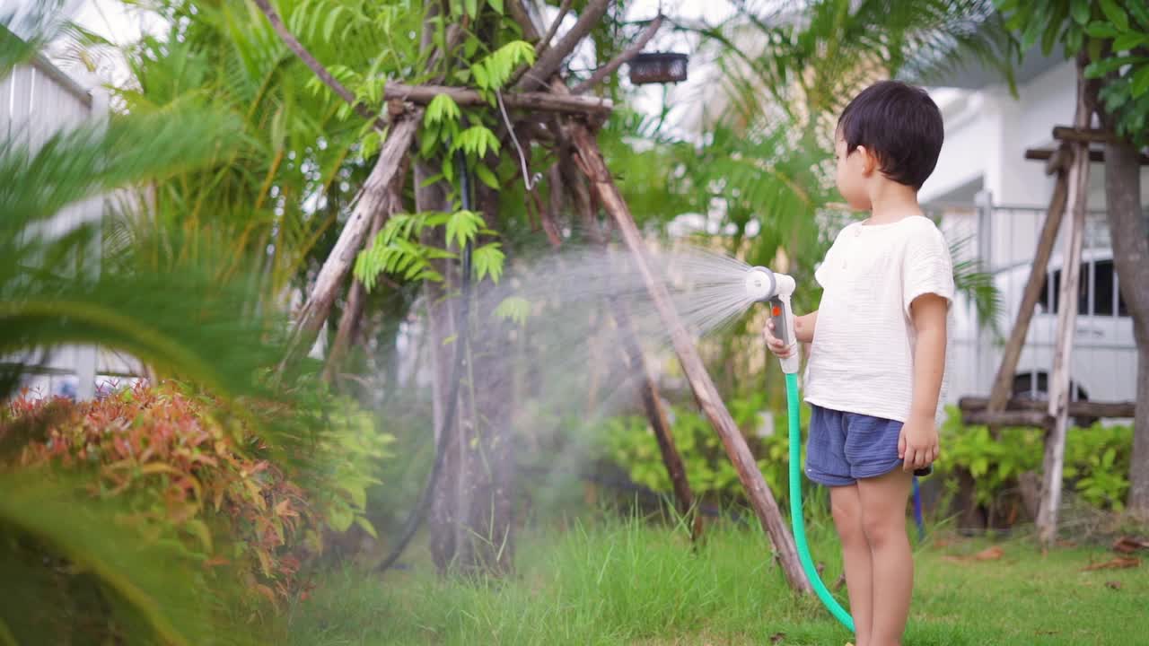 快乐的小男孩在花园里给植物和草坪洒水。视频素材