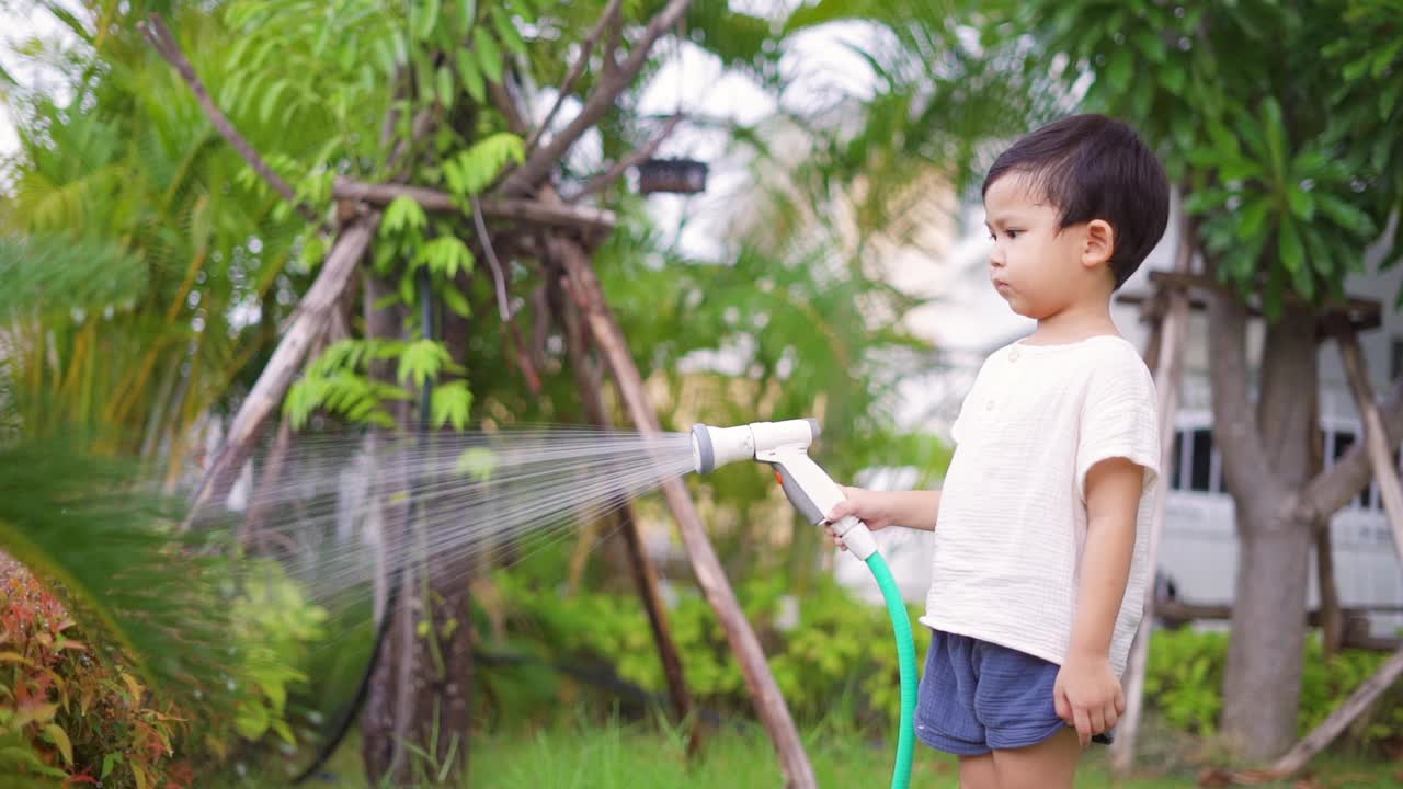 快乐的小男孩在花园里给植物和草坪洒水。视频素材