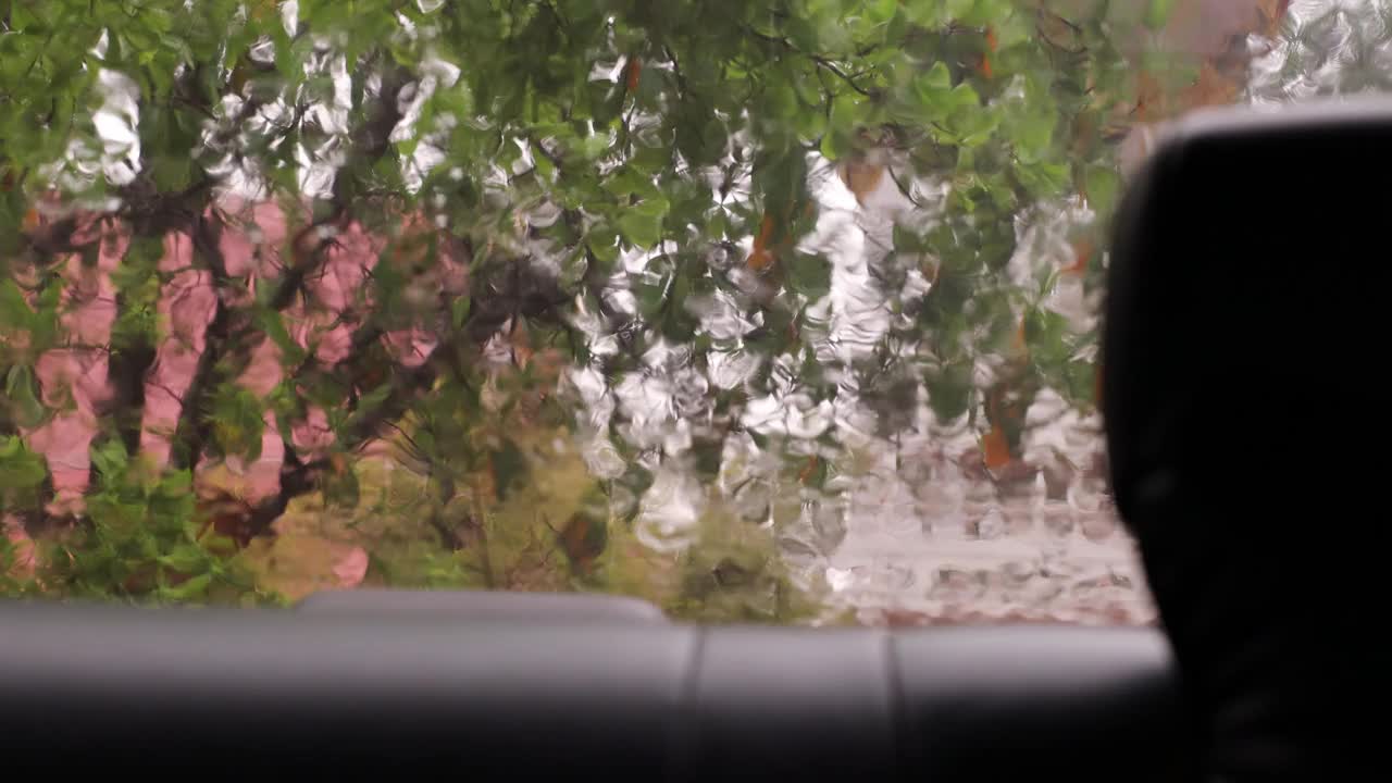 从一辆汽车的后窗里看到的景象，车上满是沉重的雨点。视频素材