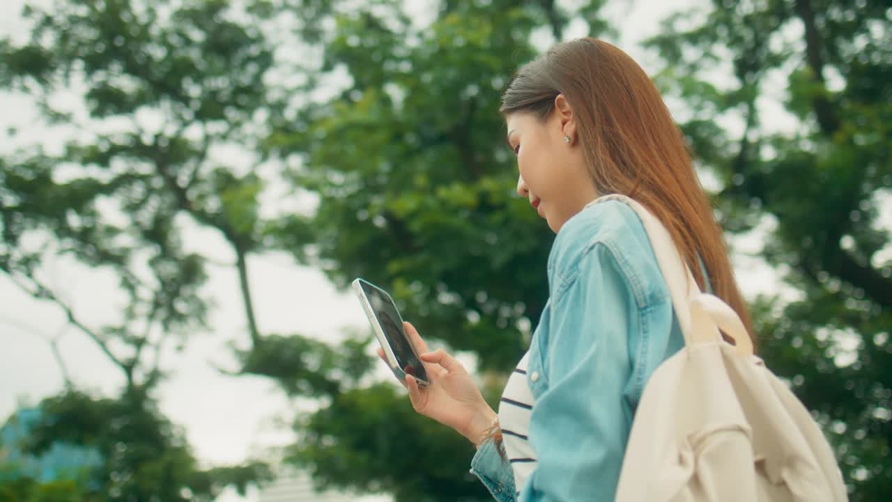 快乐的亚洲大学生在大学公园的绿树下快乐地视频通话或自拍视频素材