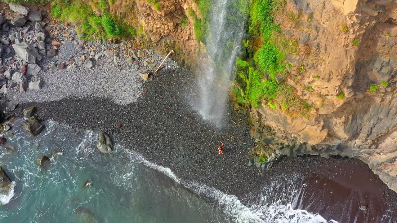 游客从马德拉岛靠近大海的山上沿着雄伟的瀑布行走的鸟瞰图视频素材