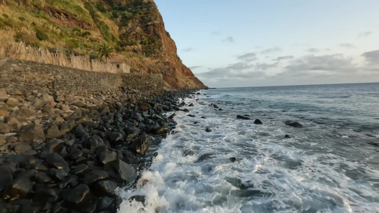 空中FPV无人机飞越海浪冲在岩石海岸在海滩上日落，马德拉岛视频素材