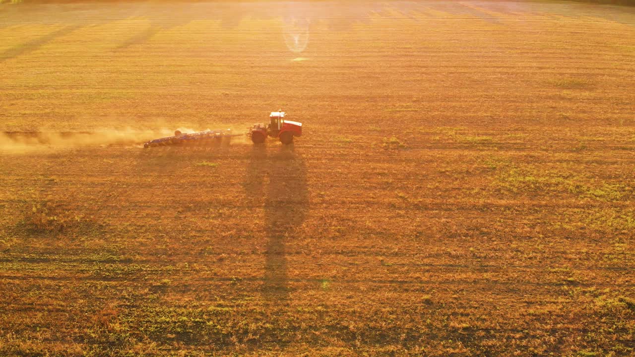 农业产业。鸟瞰图拖拉机和犁在夕阳下的田地里工作。在一个大型蔬菜农场，拖拉机用旋转犁犁地。从上面看农业。视频素材