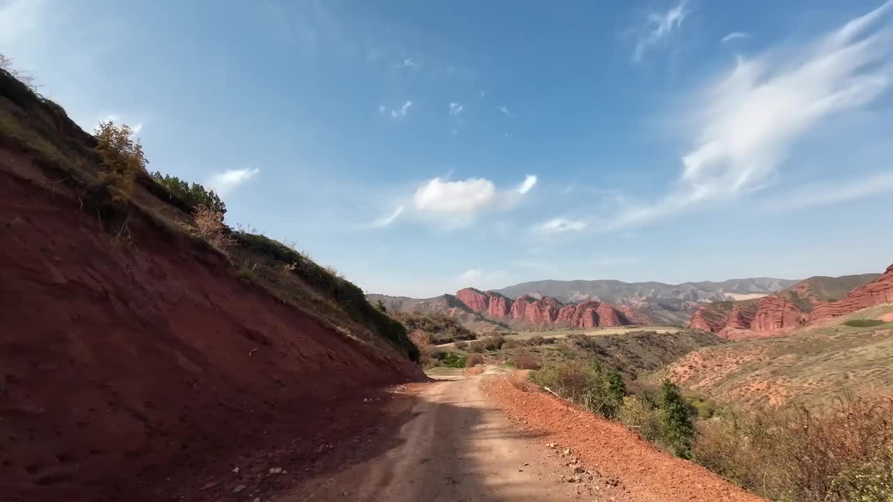 秋天，沿着红色岩石中的绿色山谷走在土路上视频素材