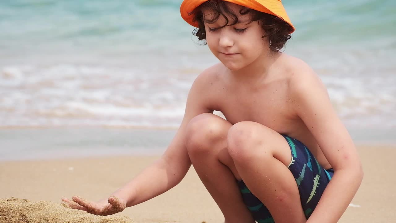 一个男孩在沙滩上玩沙子。孩子堆沙堡特写。视频下载