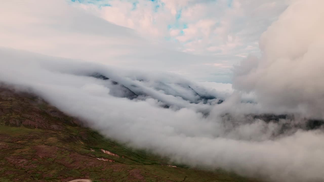 日落时分，云彩在冰岛东部的山丘上翻滚。——空中视频素材