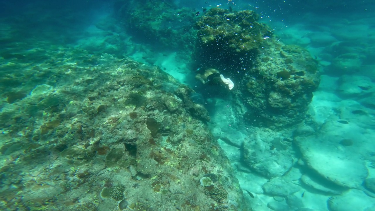 男子在蓝色的海底浮潜游泳。和一个人在海水里自由潜水。在深海中浮潜和潜水。浅水中的海洋生物。在珊瑚礁附近游泳的人慢动作4k视频素材