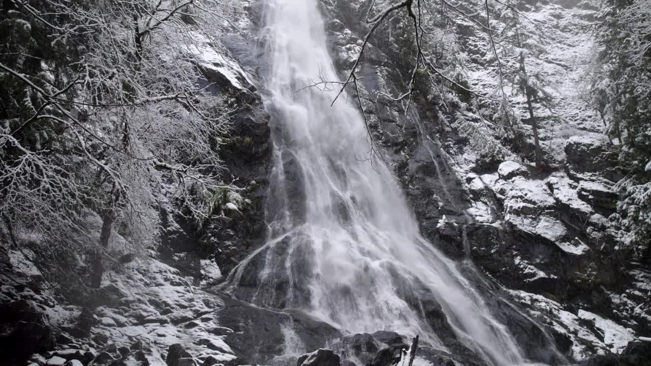 雪轻轻地落在轨道上，慢慢地穿过冬天的森林，瀑布，空中无人机视频素材