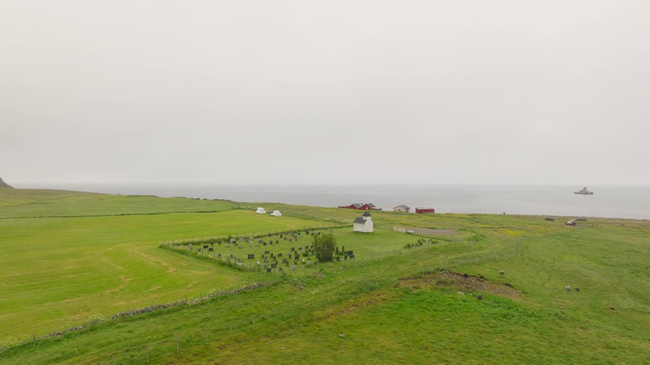 鸟瞰在挪威Vestvagoya的一个雾蒙蒙的日子里飞过Unstad教堂和Unstad墓地的鸟类。视频素材