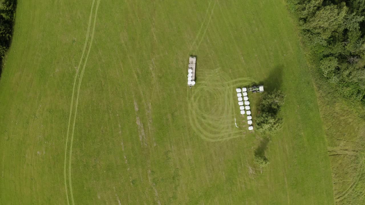 拖拉机在田野里堆垛干草卷。自顶向下的天线。视频素材