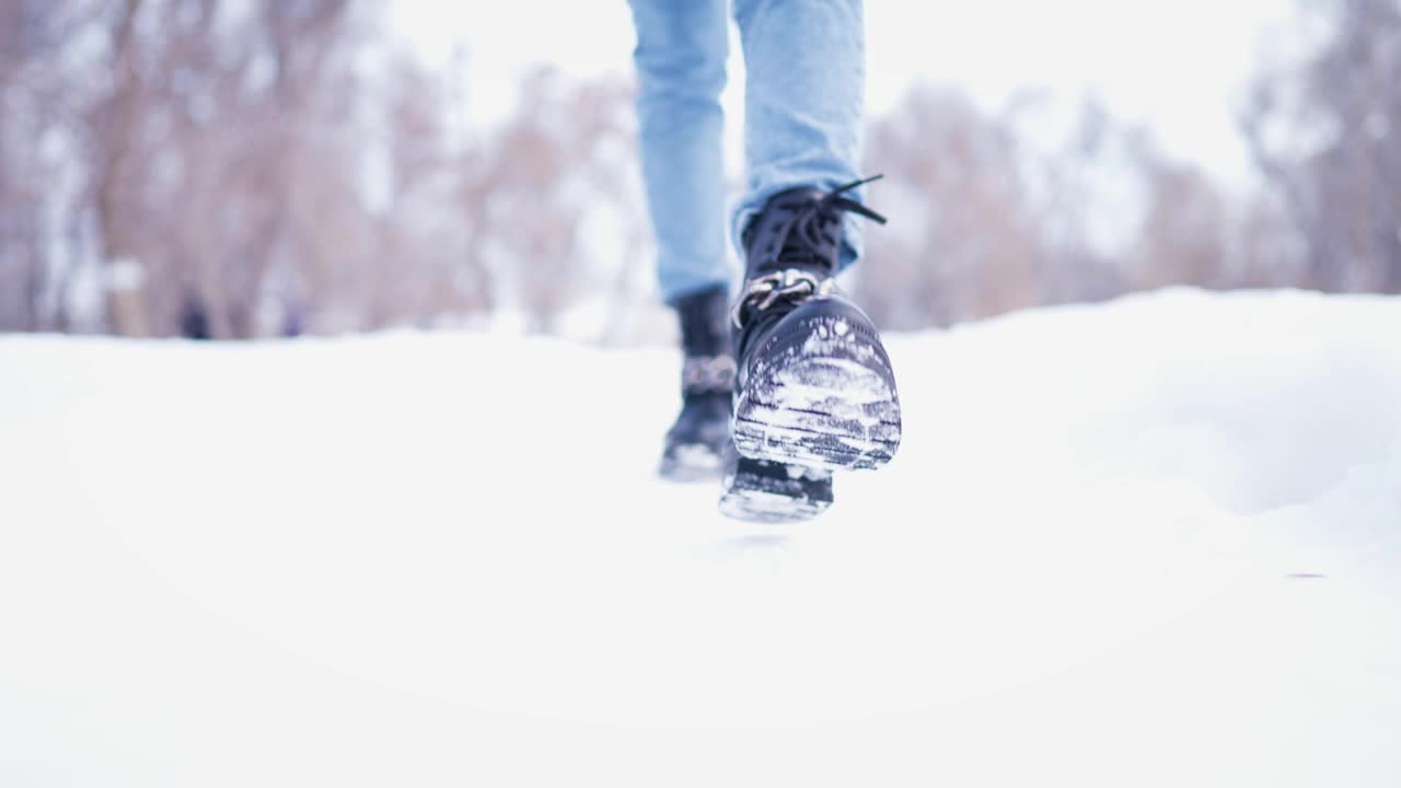 冬天下雪的公园里行走的女性腿特写。冬日里行走的女人。腿上穿着黑色的冬靴。积极的生活方式。视频素材