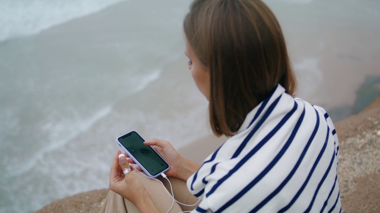 沙滩女孩在海边听音乐。思考青少年插入式耳机视频素材