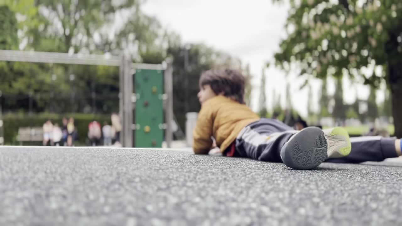 小男孩俯卧在操场的圆形平台上旋转，感受周围的环境视频素材