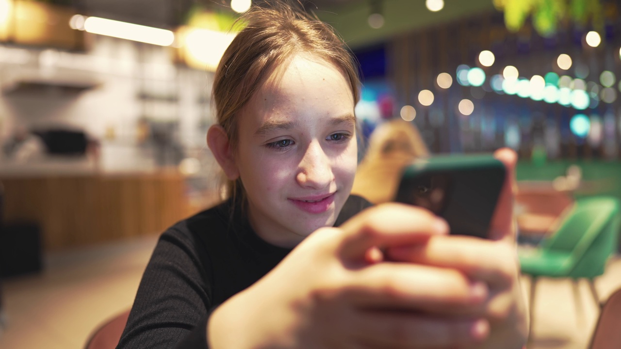 十几岁的女孩坐在路边的咖啡馆里打电话。开朗的女孩在咖啡厅的空闲时间用手机看有趣的视频。用手机聊天的女学生。视频素材
