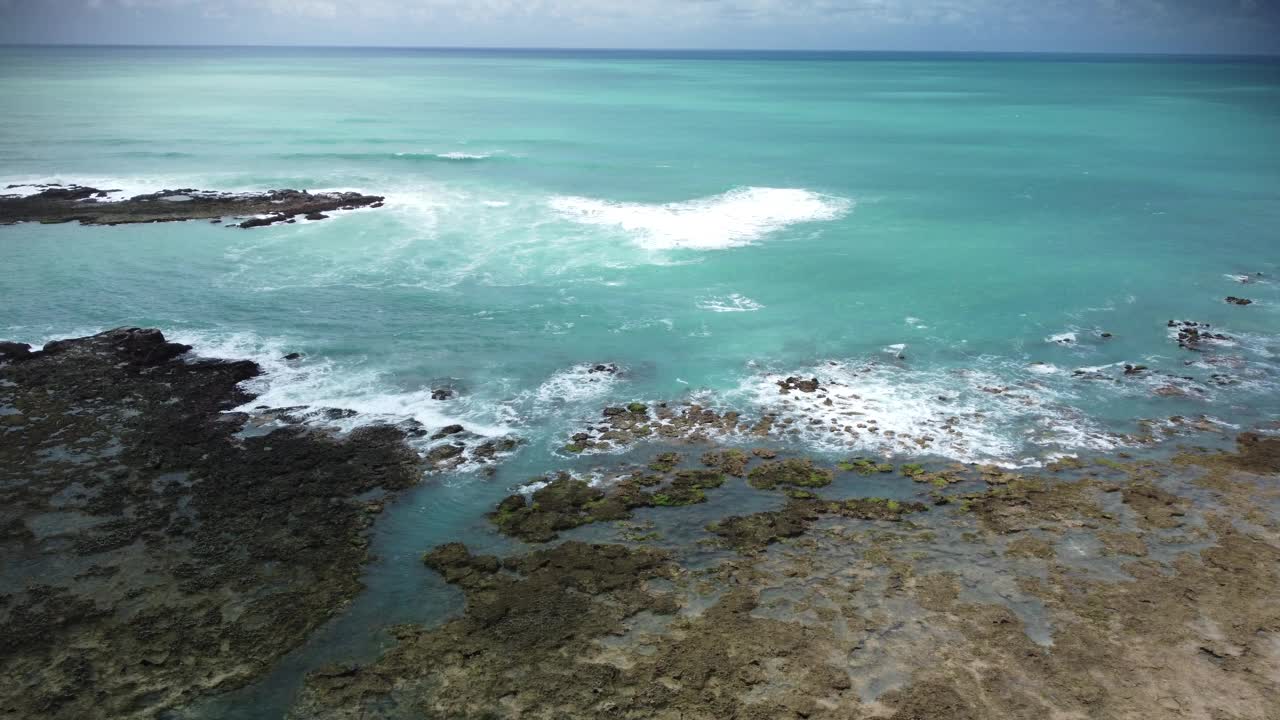 无人机拍摄的海浪在巴西阿拉戈斯州马拉戈吉的珊瑚礁湾水域撞击珊瑚的画面视频素材