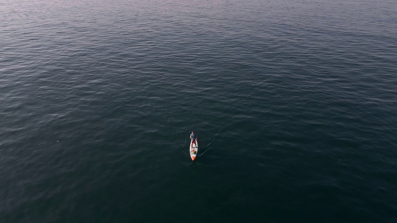 鸟瞰图，一个人在平静的海面上划着站立式桨板或SUP板。视频素材