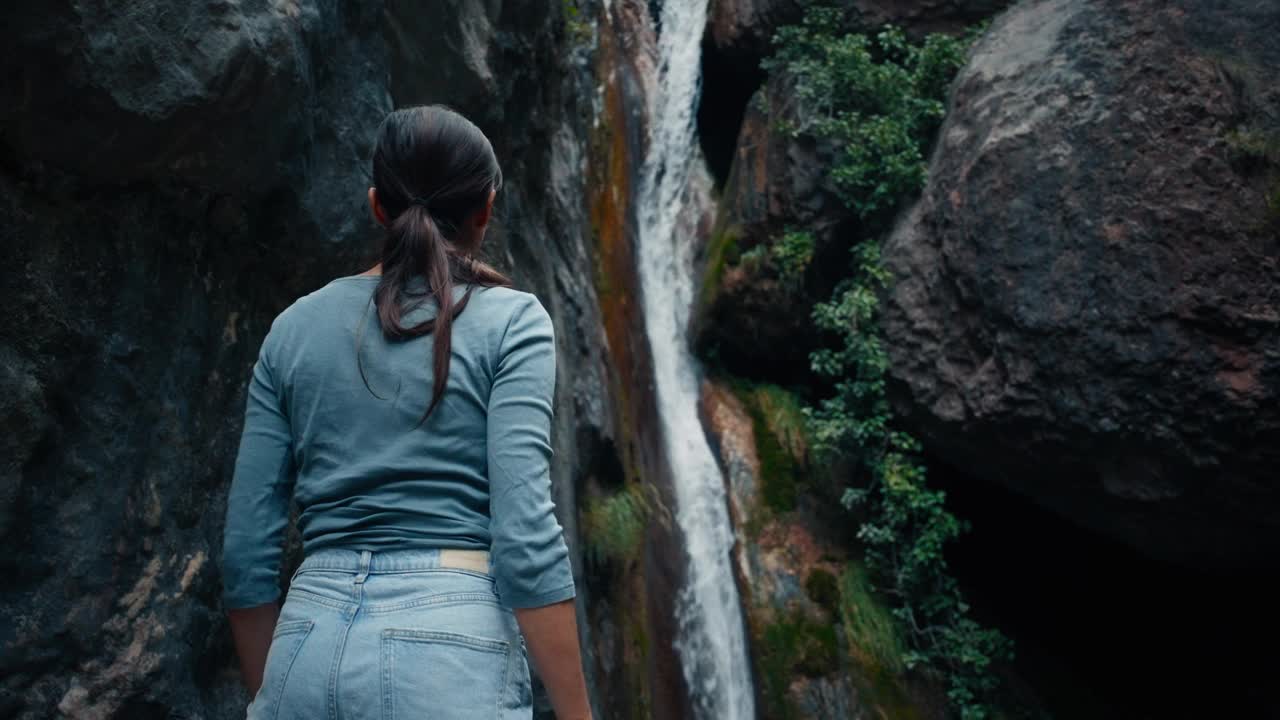 一名女游客成功地在美丽的瀑布前举起了双手视频素材