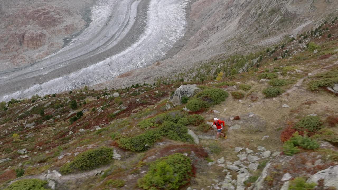 无人机拍摄的老人在高山山脊上奔跑，身后是冰川视频素材