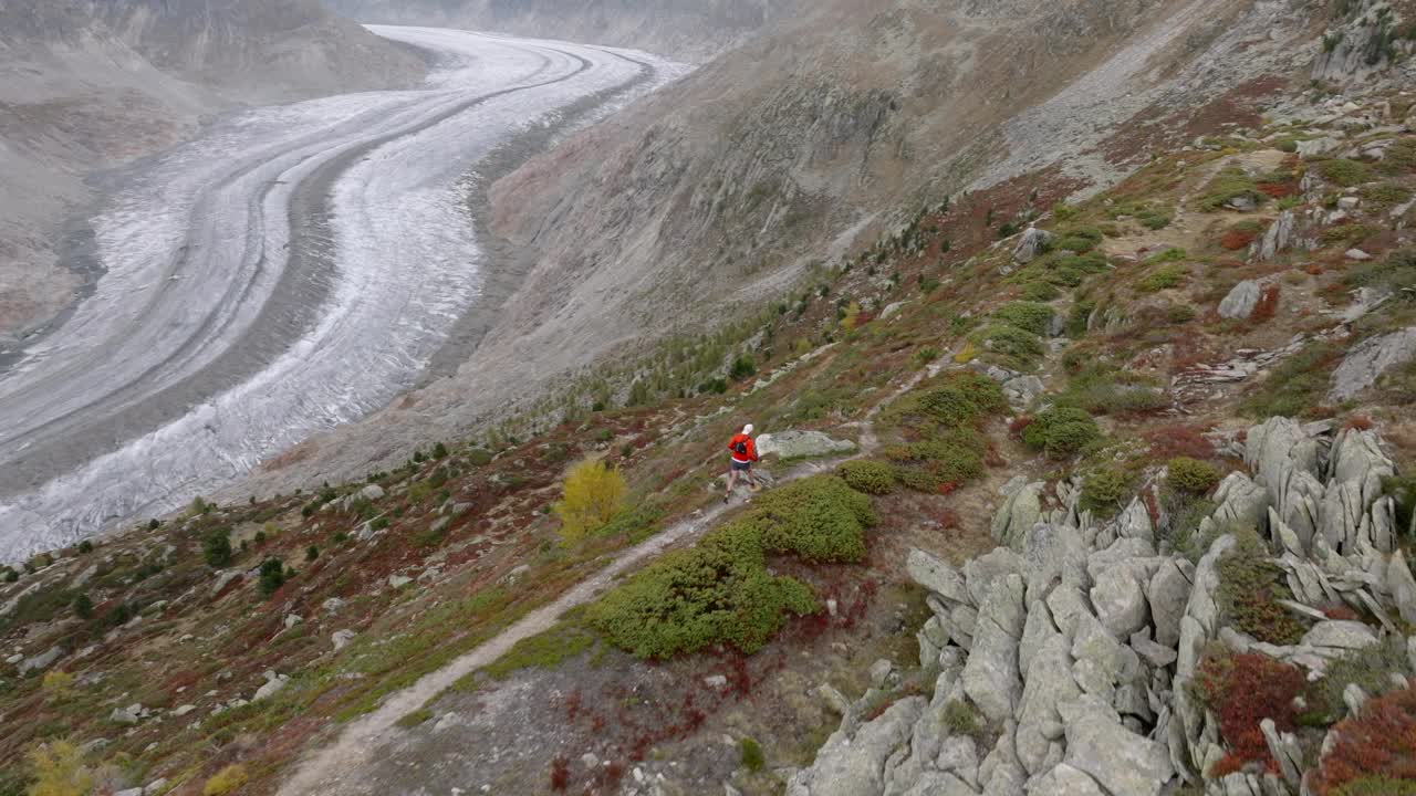 无人机拍摄的老人在高山山脊上奔跑，身后是冰川视频素材