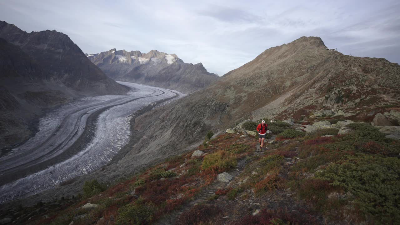 一位老人在高山山脊上跑步，身后是冰川视频下载