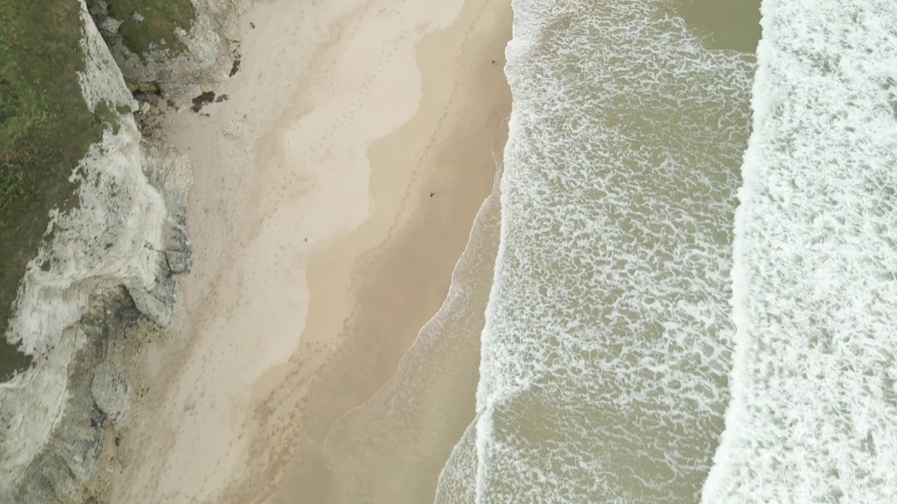 在北爱尔兰波特拉什附近，海浪冲击着白色岩石海滩的沙滩，那里有石灰石悬崖和洞穴。天线由上而下的视频素材