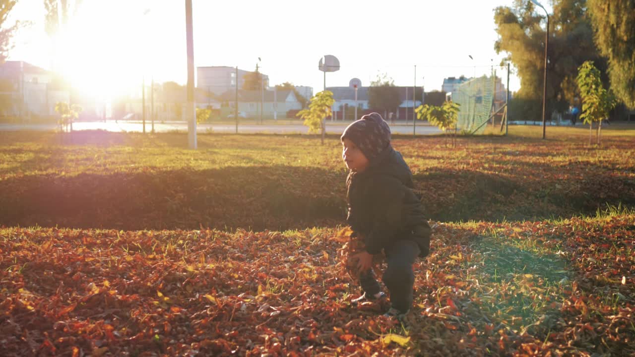 秋天走了。一个男孩在头顶上扔了一堆树叶，看着它们飘落。孩子在秋天的公园里玩金色的树叶。幸福的家庭在秋天散步。公园里的人。幸福家庭概念。视频素材