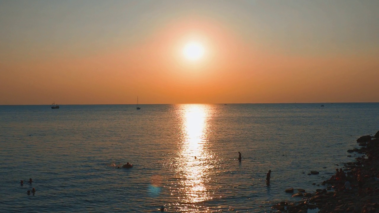 天堂海滩日出。夕阳掠过黑海，海浪冲刷着沙滩。水面上阳光明媚的小路。游客们在黎明时游泳和晒日光浴。日出，日落，黎明。旭日盘。视频素材