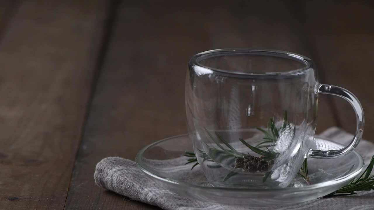 在木桌上煮热茶。将水壶里的开水倒入装有干茶的杯子里。木桌上的透明茶杯是刚泡好的茶视频素材