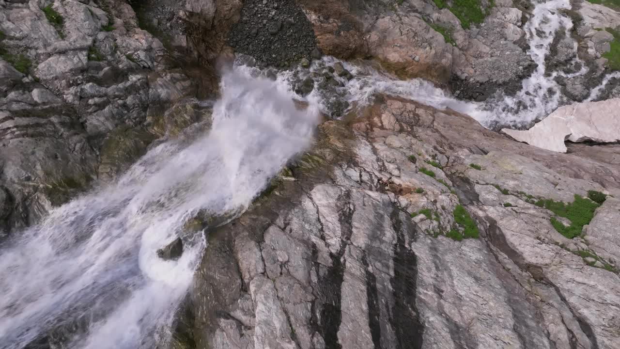 鸟瞰图近距离飞行与山瀑布从冰川流过岩石。瀑布在一个绿色的山峡谷。三轴运动视频素材