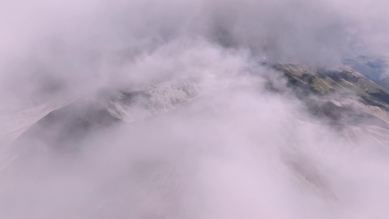 一个晴朗的下午，在山区，鸟瞰穿过空中蓬松的云层。在山和云上的真实飞行视频素材