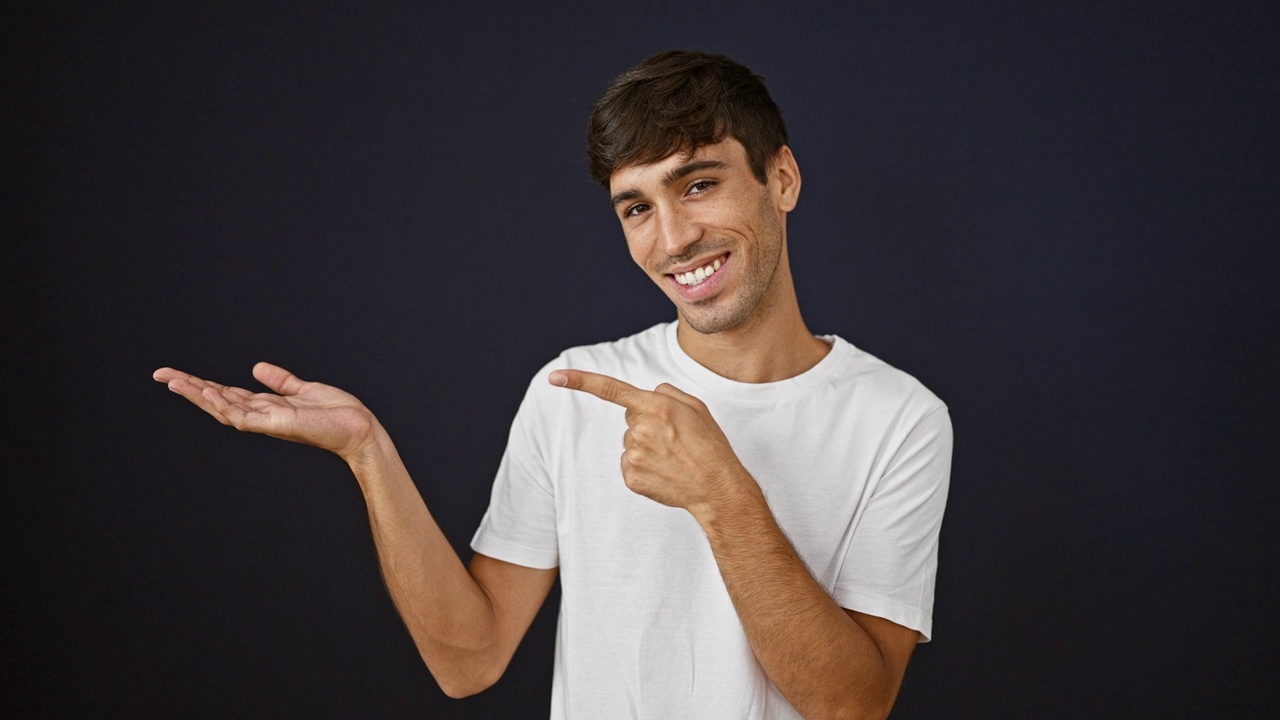 年轻的西班牙裔男子微笑着指着在孤立的黑色背景下呈现的一面视频素材