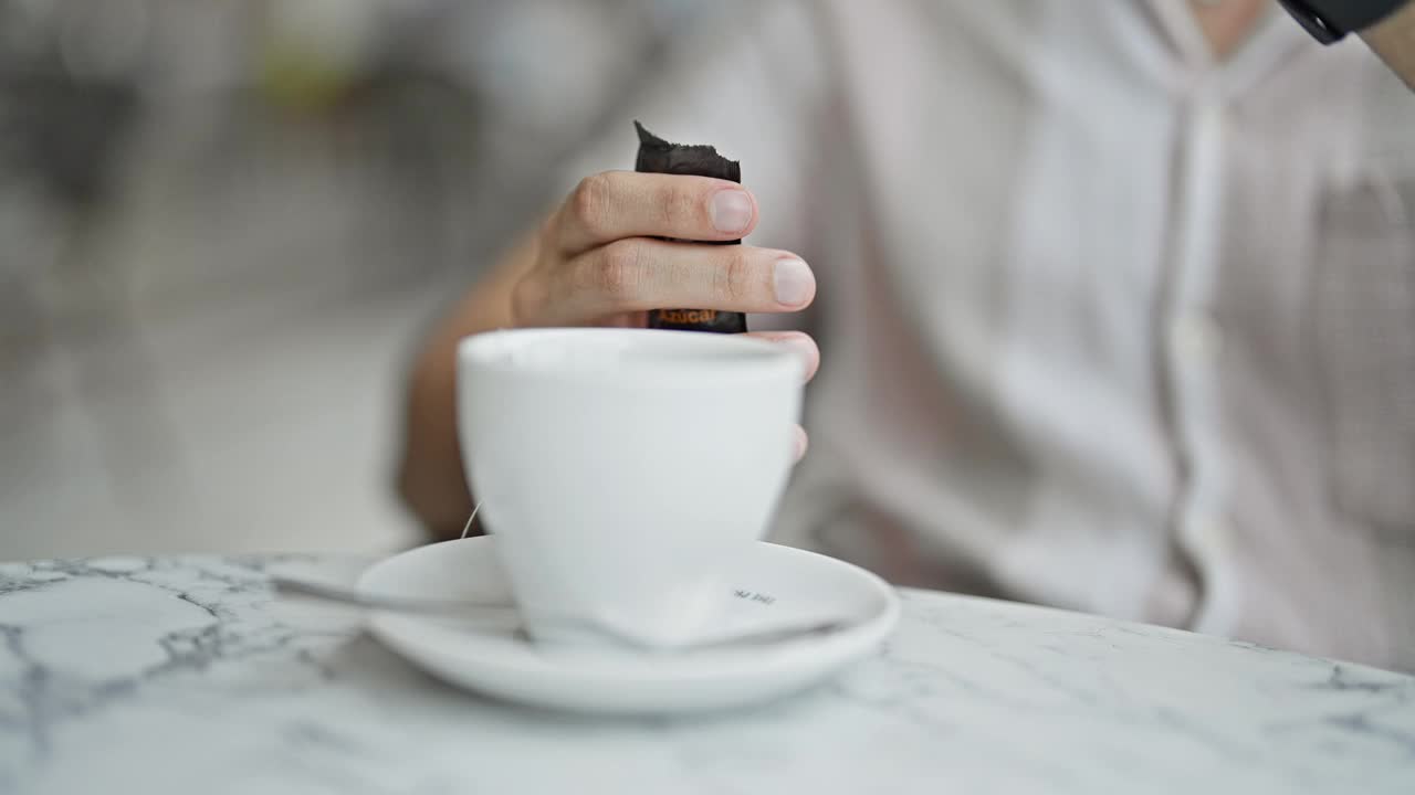 年轻的西班牙裔男子在咖啡店的露台上往茶里加糖视频素材