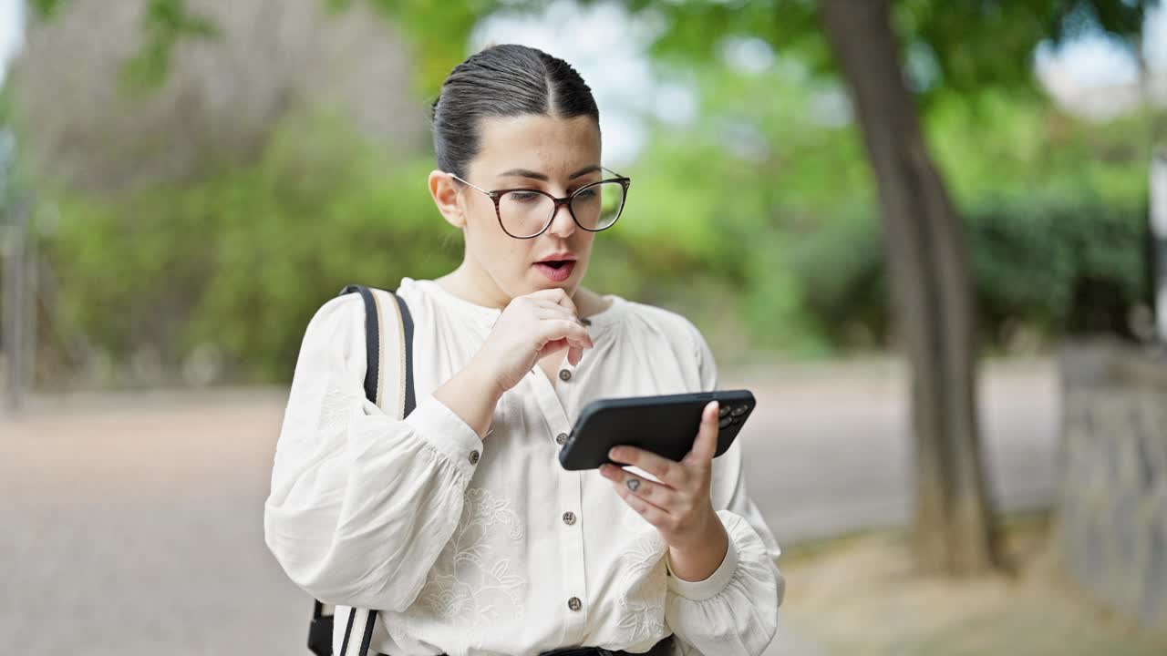 年轻美丽的西班牙女子在公园里用智能手机自信地微笑着视频素材