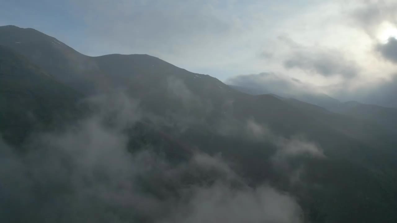 白雪皑皑的山顶上，云朵缓缓飞舞，太阳从云朵背后露出来。视频素材