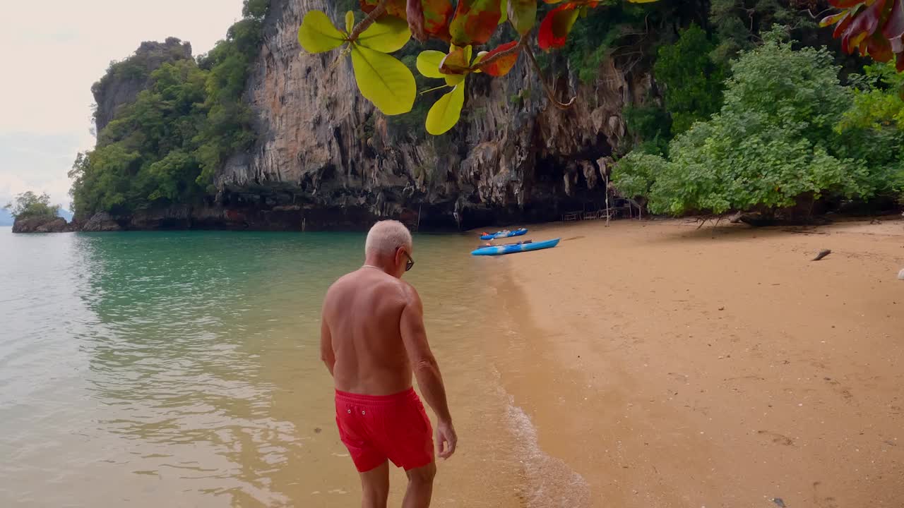 慢镜头:一个度假的成熟男人在宁静的海滩上散步视频素材