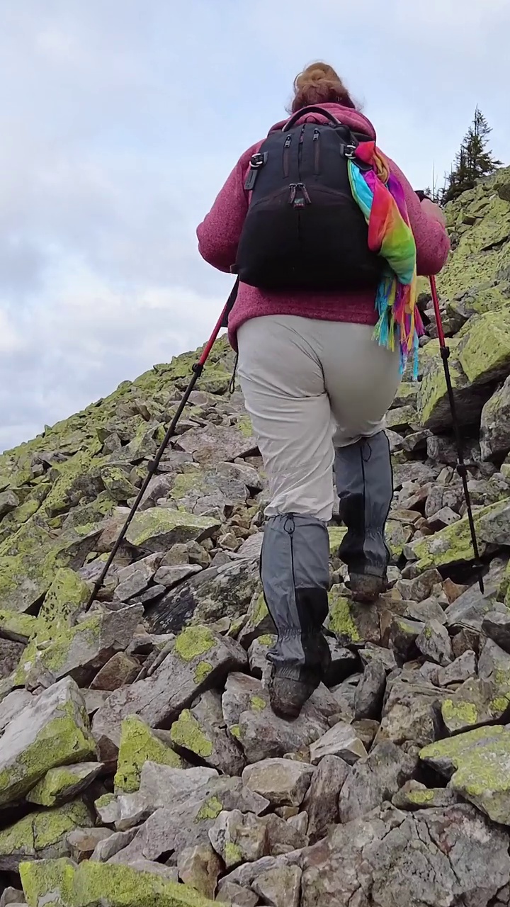 一位妇女在徒步旅行时越过岩石爬上一座山。她用登山杖视频素材