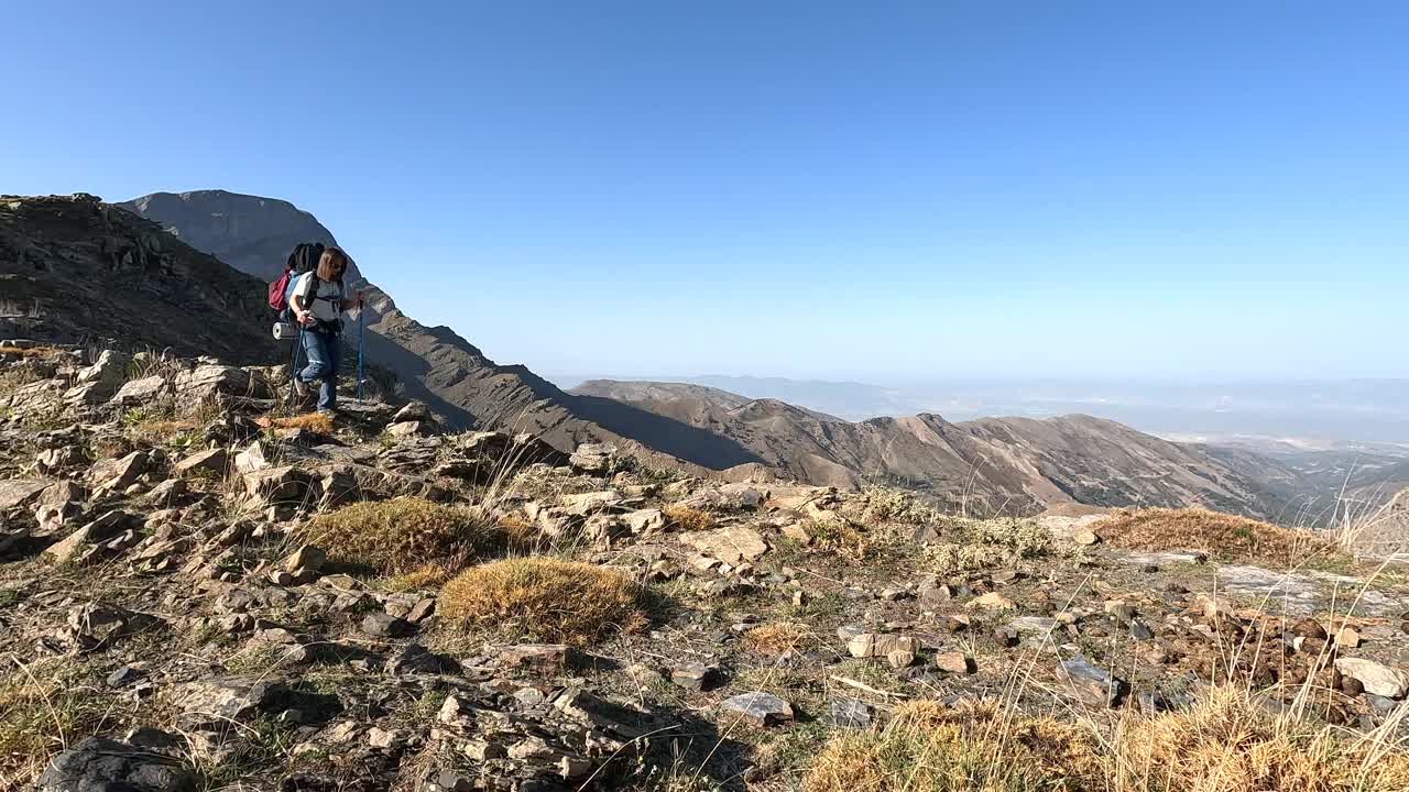 年轻的女登山者一边欣赏山峰的美景，一边向山顶走去。视频素材